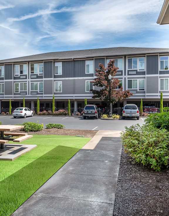 A grey building with a tree in front of it. at Fairview Village Apartments, Fairview, Oregon