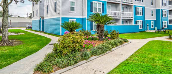 a gray and blue apartment building with a garden in front of it
