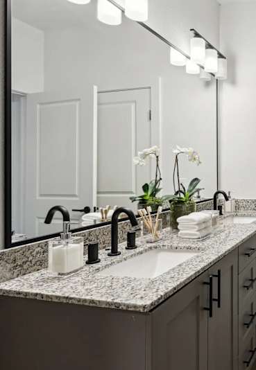 A bathroom with a large mirror, a sink, and a towel hanging on the door.