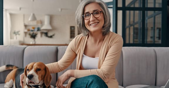 A woman is sitting on a couch with a laptop and a dog.