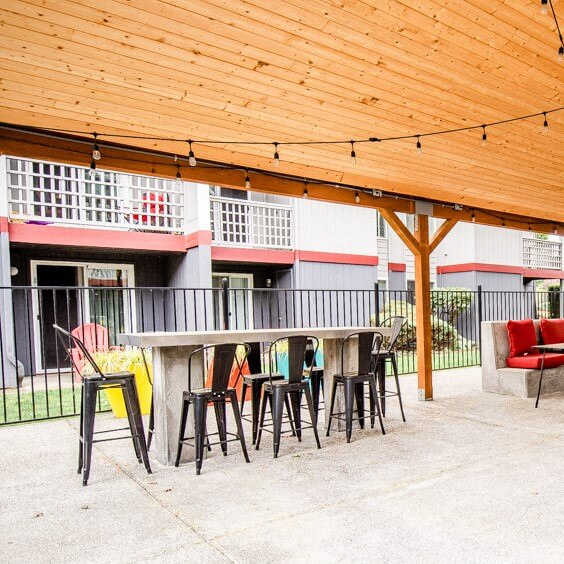 A wooden patio with a table and chairs under a roof.