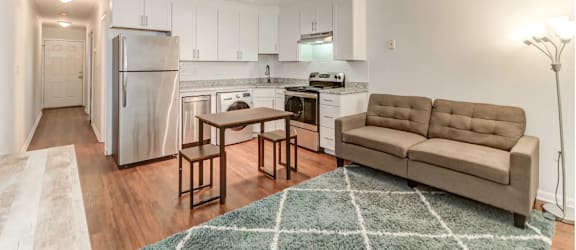 a living room with a couch and a kitchen with a refrigerator