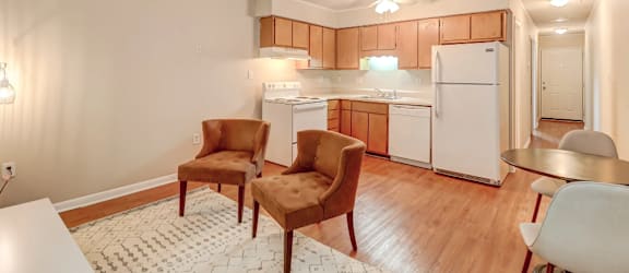 a living room with two chairs and a kitchen with white appliances