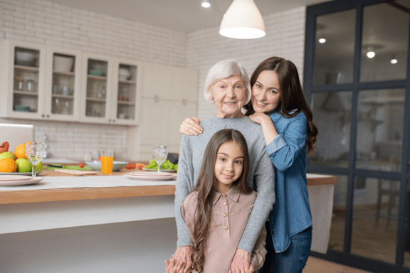 A woman and a young girl are hugging an older woman in a kitchen.