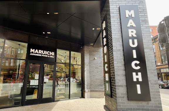 The exterior of a Maruichi store with a black and white sign.