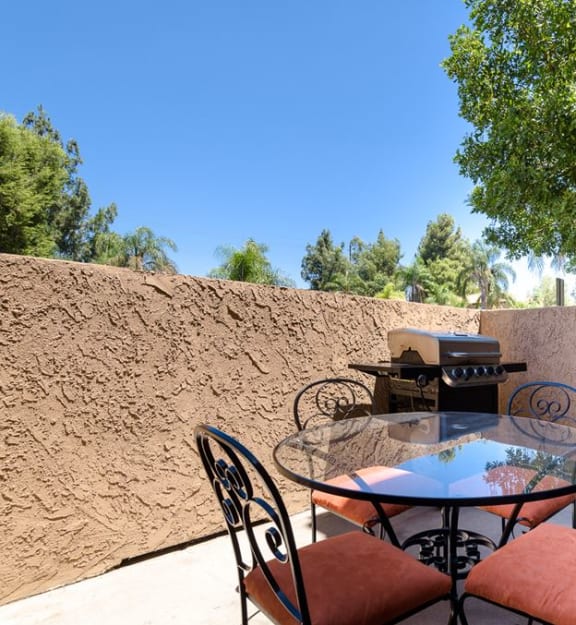 a patio with a glass table and chairs and a grill