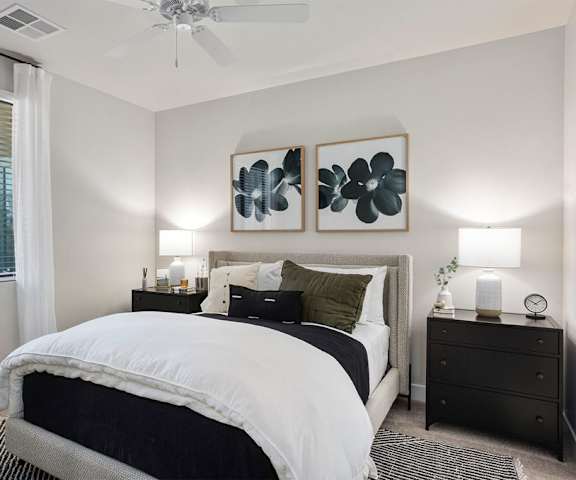 A cozy bedroom with a queen-size bed, a dresser, decorations, window, lamps, and nightstands at Reflect at Dobson Ranch Apartment Homes. 