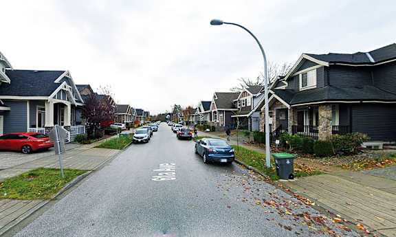 A street with cars parked on the side and houses on both sides.