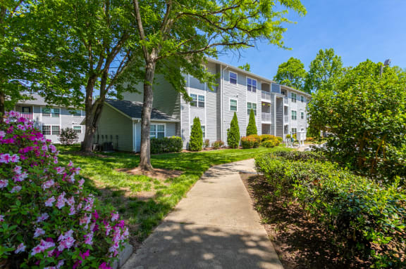 A pathway leads to a building with a green lawn and trees at West Pointe Apartments in Burlington, NC