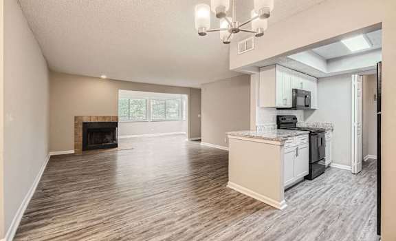 A living room with a fireplace and a kitchen area in the background.