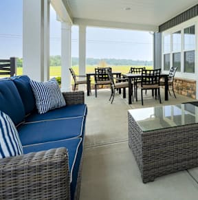 A blue couch with striped pillows sits on a patio with a glass table and chairs.
