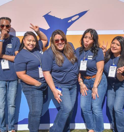 A group of people in blue shirts are standing in front of a blue and orange background.