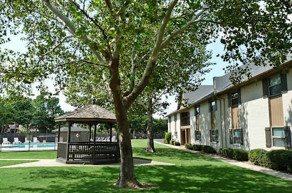 A tree stands in front of a building with a gazebo in the foreground.