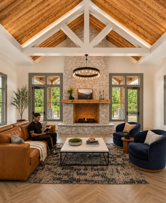 A man is sitting on a brown couch in a room with a stone fireplace and a chandelier.