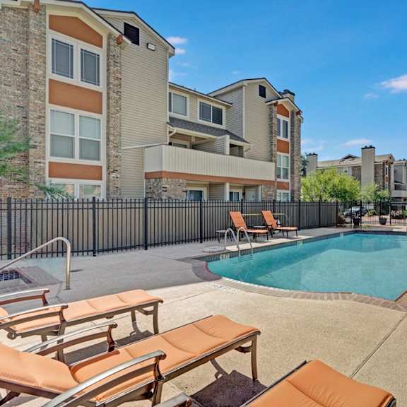 The large, turquoise, fenced-in, outdoor pool with pool chairs with the apartments in the background at Summertree Place Residences. 