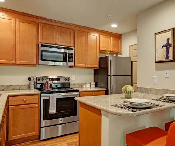 A large kitchen with stainless steel appliances, marble countertops, and large wooden cabinets at Windsong Apartment Homes. 