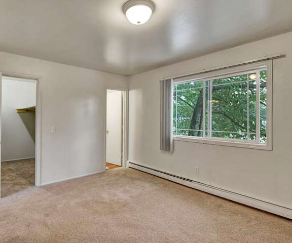 A large, empty carpeted bedroom with overhead lighting and a window at the Village at Calais Apartment Homes. 