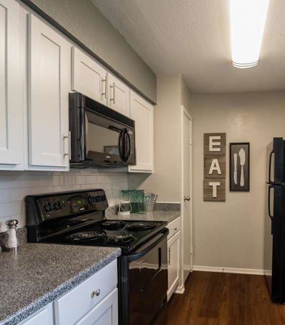 A kitchen with grey countertops, dark wood floors, and black appliances.
