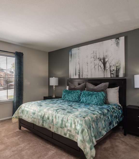 A bedroom at Fusion Crossroads Apartments with a grey accent wall, blue curtains, and a blue bedsrepad.