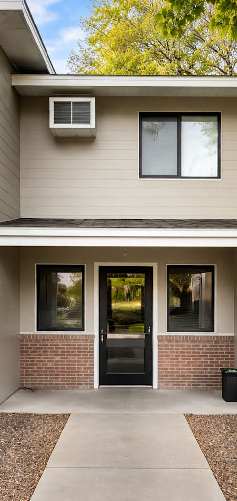 A two-story house with a grey siding exterior and a red brick base.