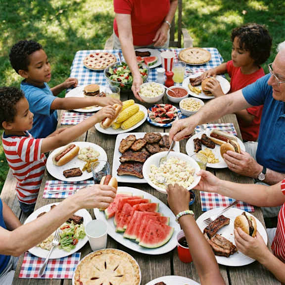 A group of people are gathered around a picnic table full of food.