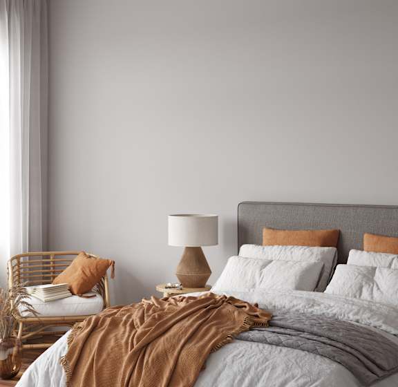 A bed with a grey headboard and white pillows is covered with a brown blanket.