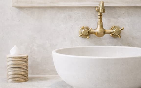 A white porcelain sink under a mirror with a gold faucet.