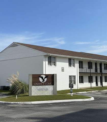 A white building with a sign that says "Osprey Cove" in front of it.
