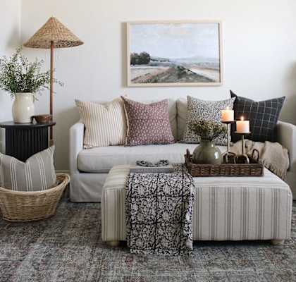 A living room with a couch, a table with a basket, a candle, and a painting on the wall.