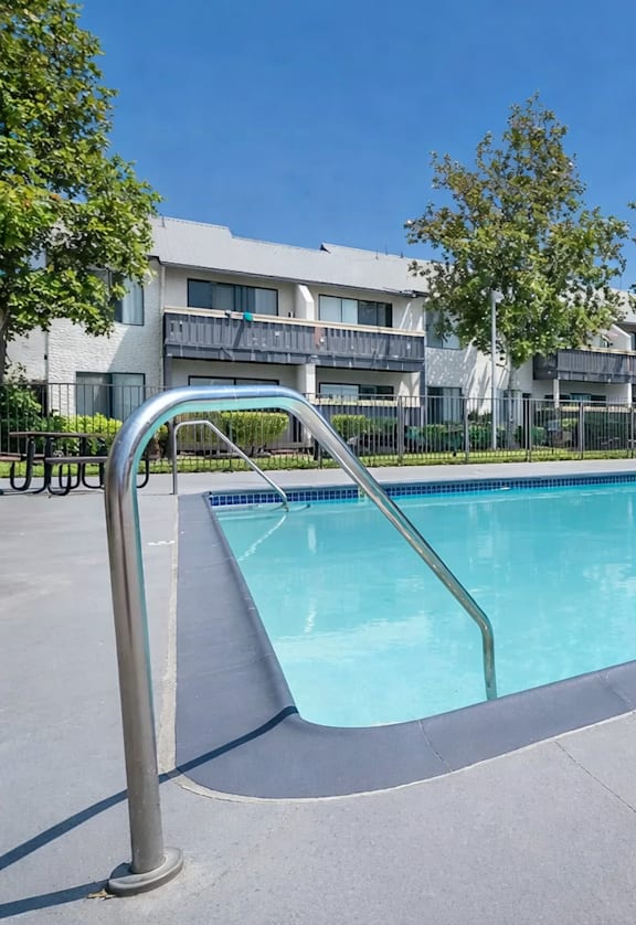 A swimming pool with a ladder in the foreground and apartment buildings in the background.