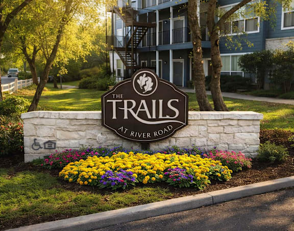 The Trails at River Road sign is in front of a building and trees.