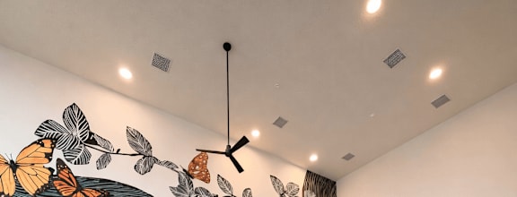 Modern apartment fitness center with high ceilings, large windows, cardio equipment, strength machines, and a butterfly mural accent wall.