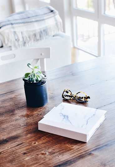 Small potted plant on a wooden table beside a book and glasses, creating a cozy living space at Eden West Apartments.