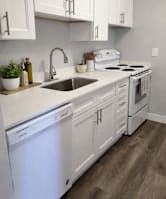 A white kitchen with a dishwasher, sink, and stove.