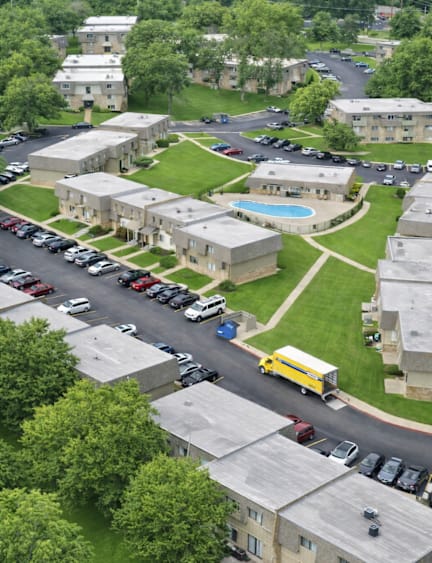 A parking lot with cars and a yellow truck in front of a building with a pool.