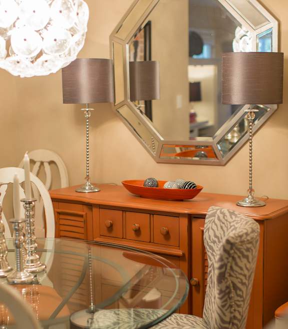 A chair with a zebra print upholstered back sits in front of a desk with a mirror and two lamps.