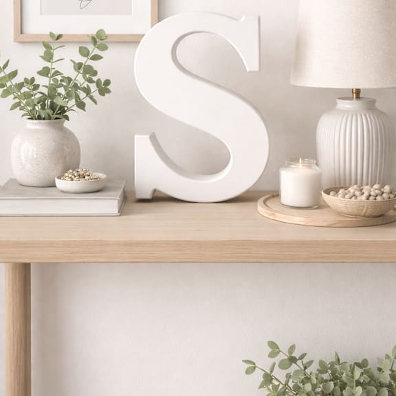 A white letter S is on a table with a plant, a candle, and a vase.