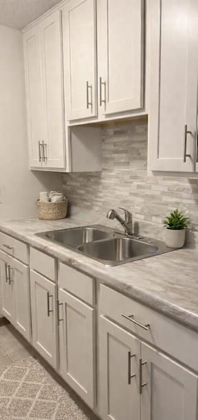 A kitchen with a black refrigerator, white cabinets, and a marble countertop.