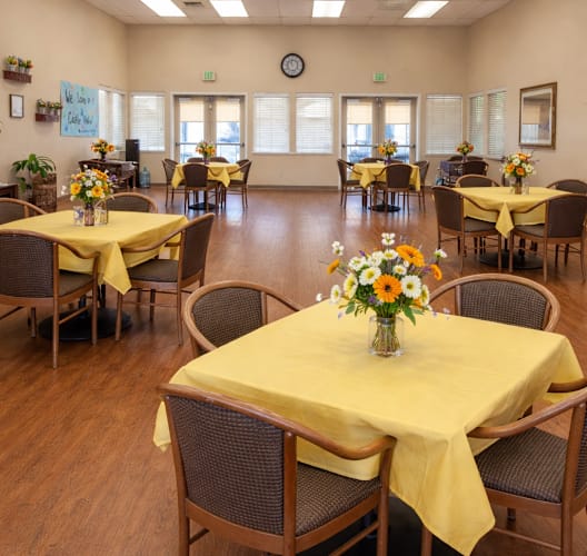 A dining room with tables covered in yellow cloth and chairs around them.