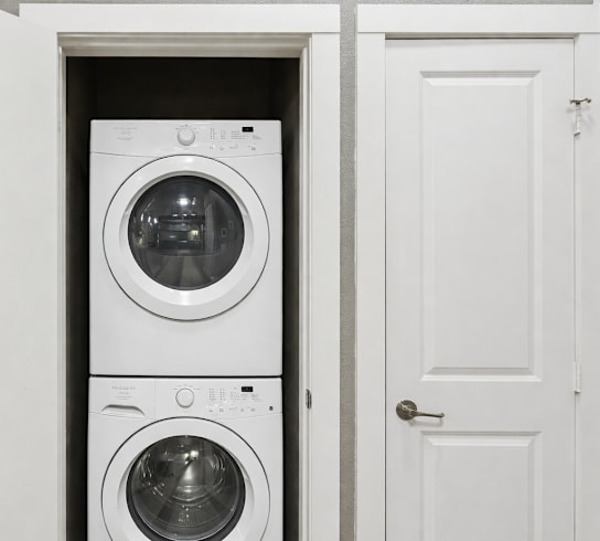 A white door is open to reveal a white washing machine in a laundry room.