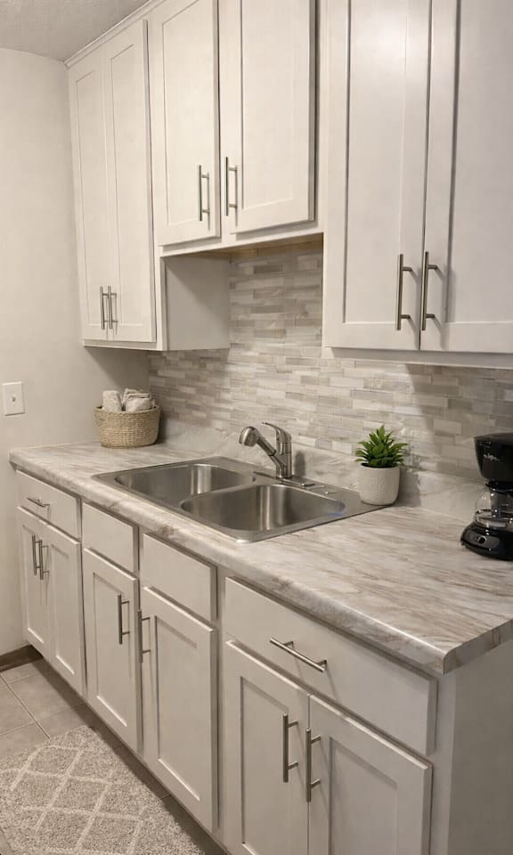 A kitchen with white cabinets and a marble countertop.