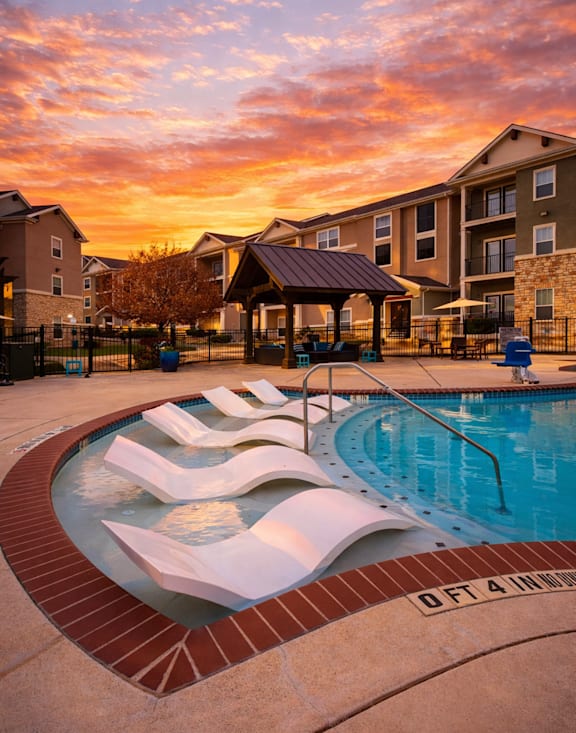 A swimming pool with a slide in front of apartment buildings during sunset.