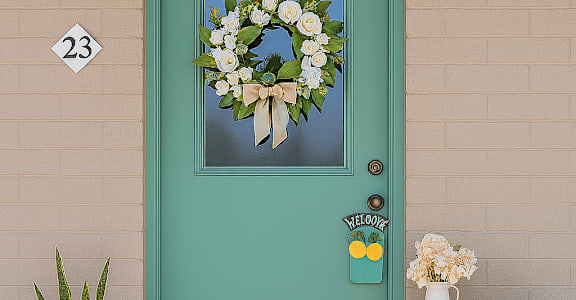 A green door with a wreath and two potted plants.