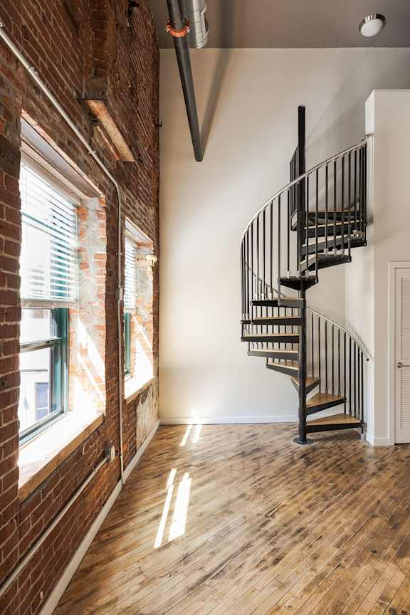 A wooden staircase with a metal railing is in a room with a brick wall and a window.