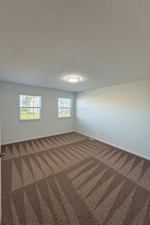 A room with carpeted floor and two windows.
