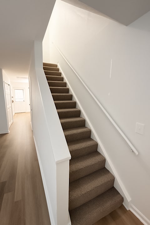 A staircase with a white railing and brown carpeted steps.