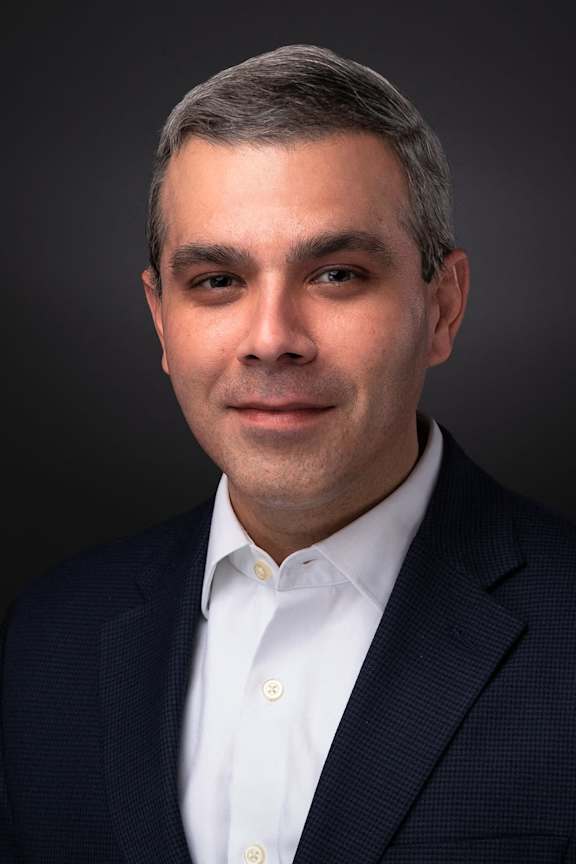 A man with short grey hair wearing a dark blue suit and white shirt.