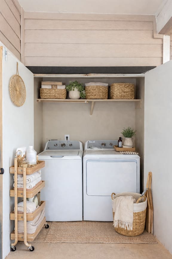 A laundry room with a washer and dryer, a basket on the floor, and a rack with towels.