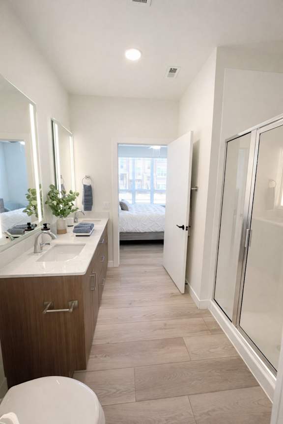 A bathroom with a toilet, sink, mirror, and a plant.