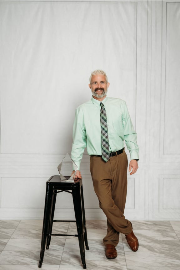 a man in a shirt and tie standing next to a stool